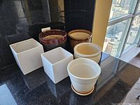 View of the six ceramic flower pots arranged together showing variety of shapes and colors on black countertop with city view background