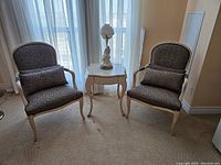 Two matching upholstered side chairs flanking marble-top side table with decorative lamp on top