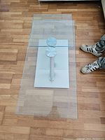 Top-down view of rectangular coffee table with clear glass surfaces, chrome supports, and white base on wooden floor.