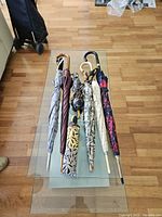 Seven umbrellas displayed on a glass table, showing variety of sizes, handles, and fabric patterns.
