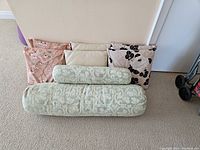 Overall view of 8 cushions: 3 square floral, 2 plain beige, and 2 cylindrical damask bolsters.