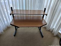 Front view of computer desk with curtain background showing two-tier shelves and black metal frame.