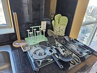 Wide view of cooking accessories on kitchen counter including oven mitts, utensils, glass cutting boards, citrus juicer, and paper towel holder.