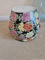 Barrel-shaped ceramic flower pot with colorful flowers on black background, showing overall detail.