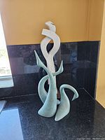 Photo showing the abstract white marble statue with curved design elements and the set of three light green ceramic swan silhouettes grouped together.