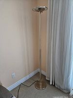 Full view of brass halogen floor lamp standing beside a wall and curtains, showing height and cord base.