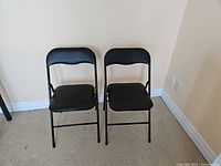 Two black folding chairs with padded seats and backs shown side by side.
