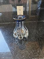 Glass vase with blue rim and bulbous teardrop shapes, shown on a granite surface near electrical outlet