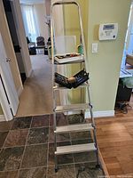 Full view of silver aluminum utility ladder with four steps and blue rubber feet; platform holds tool case with assorted tools.