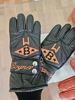 Black leather Bocner gloves with orange branding and snap closure, laid flat.