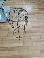Photo of the metal plant stand showing its height and decorative side details on a wooden floor.