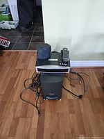 Full Bose 3.2.1 GSX system components including subwoofer, DVD main unit, two satellite speakers, remote control, and cables arranged on floor with wooden flooring background.