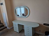 Light mint lacquered wood vanity desk with 10 drawers paired with oval mirror on the wall.