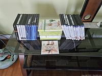Top-down view of all 33 yoga DVDs arranged on a glass table, including some stacked horizontally and others vertically.
