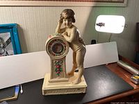 Antique chalk ware figural clock with cherub figure beside clock face, showing overall front and left side view.
