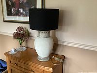 Lamp on wooden dresser with black cylindrical shade, showing overall appearance and lamp cord.
