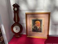 Wide view of the vintage barometer and the framed print side by side on a red surface against white wall