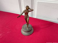 Full view of the bronzed figurine showing the dancer on the ornate round base, showcasing the detailed painting and posture.