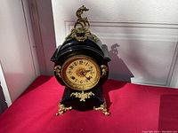 Full front view of clock on red surface showing black case and brass decorations