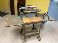 Front view of Delta scroll saw mounted on metal stand with drop-down sides and wheels.