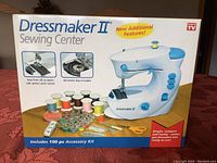 Box showing Dressmaker II Sewing Center with spools of thread, bobbins, and accessories laid out