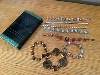 All items displayed including the black and green vintage tin box, and a variety of bracelets arranged on a wooden surface.