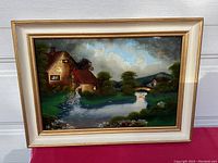 Full view of the framed reverse painted glass artwork showing a rural scene with a house, river, and bridge.