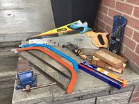 Entire tool lot arranged on concrete surface, showing vice, saws, sharpening stones, rivet tool in original packaging.
