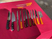 Full view of all knives and sharpening tools laid out on red surface, showing a variety of blades and Bakelite handles.