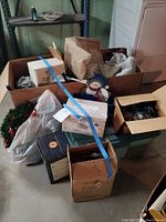 Boxes and containers with various Christmas decorations including ornaments, lights, and holiday themed items in a cellar setting.