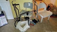 Wide view photo of shower chair, quad canes, toilet booster seat, grabber, shoehorn, knee brace, heating pad, part of walker, and pulse oximeter on floor.