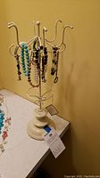 White metal jewelry stand with various bracelets hanging from hooks, photographed against a yellow wall on a light surface.