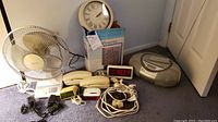 Overview photo showing all items: 2 fans, 3 clocks, boom box, 2 phones, cords, and wall clock.