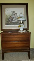 Photo showing the nightstand with two wooden drawers and dovetail joints, topped with the lamp and the framed Bengal cubs print in the background.