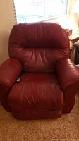 Front view of the deep red power recliner chair showing padded seat, armrests, and cushioned back with wear on seat and armrest.