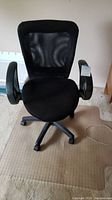 Front view of black rolling desk chair on beige textured floor mat.