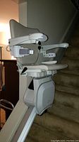 Side view of Handicare 1100 stairlift chair installed on carpeted stairs, showing armrest controls and rail.