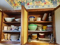 Wide view of wooden cabinet shelves containing various dishes including mugs, plates, bowls, and plastic containers stacked neatly.