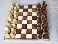 Full view of the assembled chessboard with white and brown alabaster squares, framed in gold, with complete set of alabaster chess pieces lined up on all sides.