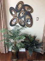 Photo showing both artificial plants below decorative oval mirror wall art.