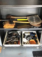 Top shelf showing two axes, one sledge hammer, scrap wood pieces and a hand saw.
