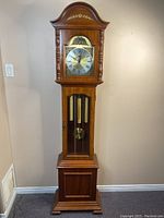Full view of the grandfather clock standing against a wall showing its height and wooden finish.