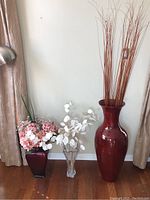 Overview of three vases with artificial flowers and reeds against wall with curtains