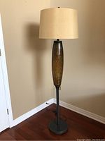 Full view of the floor lamp showing entire height, metal base, blown glass body, and fabric lampshade.