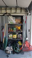 Full front view of gray utility cabinet filled with various garden supplies including hose, rakes, chemicals, gloves, and watering can.