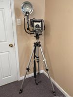 Full view of Graflex Speed Graphic camera mounted on Manfrotto tripod with flash attached