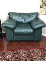 Front view of green leather arm chair placed on wooden floor near decorative rug and wall art.