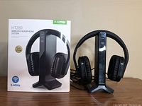 Photo of Avantree HT280 wireless headphones on charging dock next to the product box, showing front view.