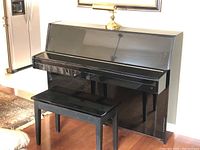 Front view of black high-gloss upright piano with bench and brass lamp on top