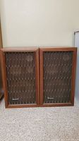 Pair of Kenwood speakers side by side showing wooden frames and front grille with lattice design.